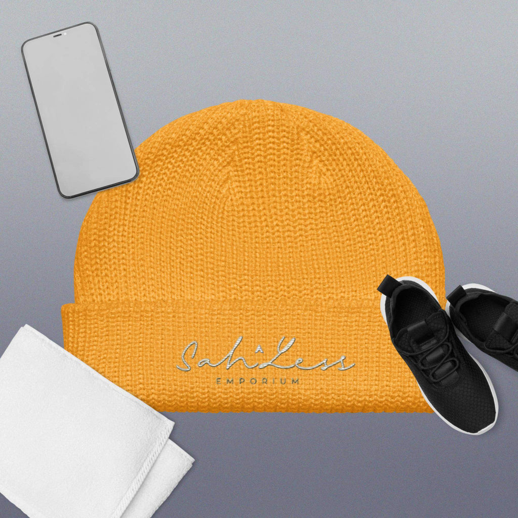 Fisherman beanie in mustard yellow with SahLess Emporium logo, placed with a phone, towel, and black sneakers.