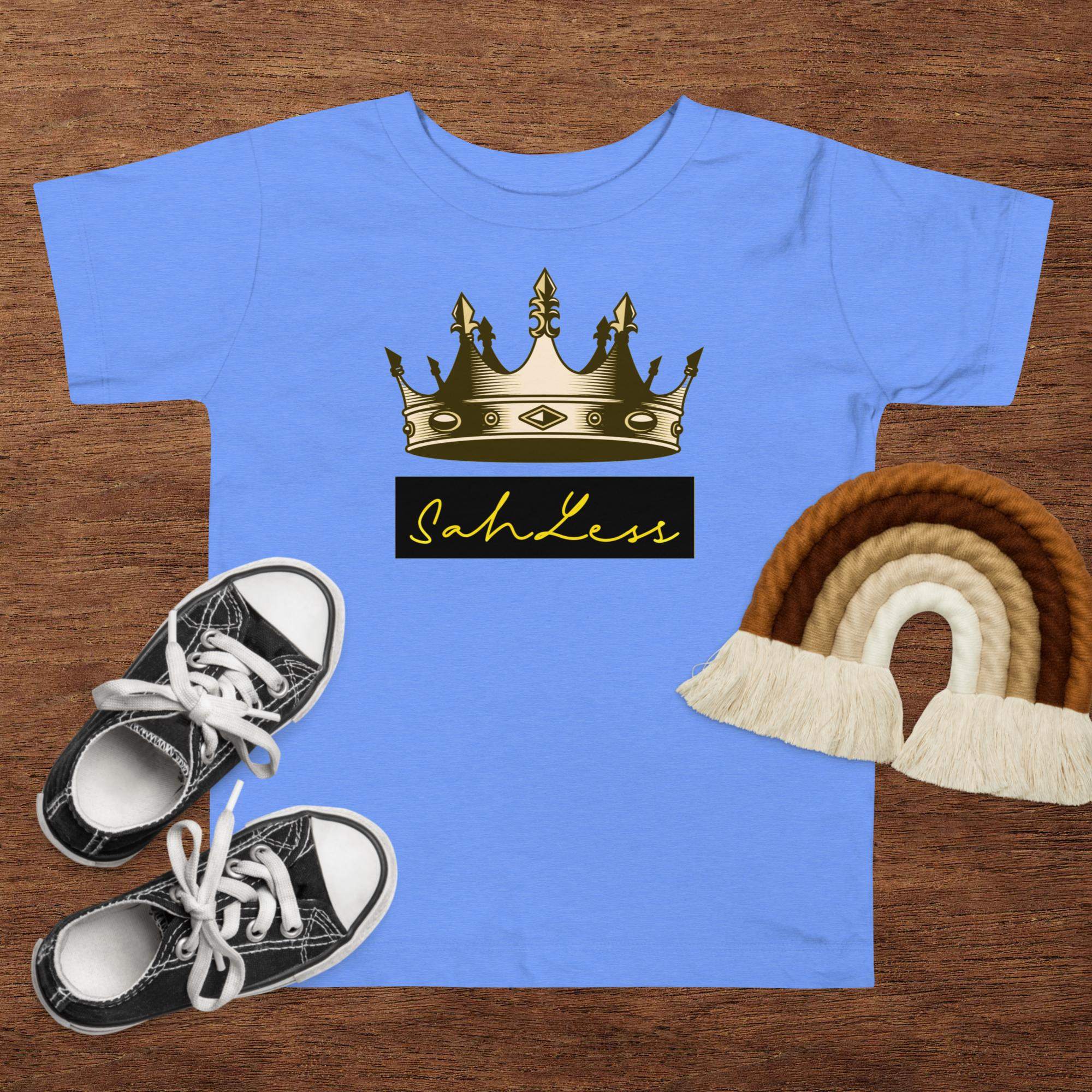 Toddler short sleeve tee with crown print on a wooden surface with shoes and decor.