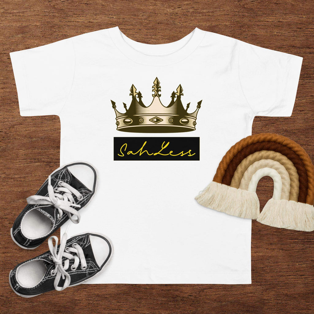 Toddler short sleeve tee with crown graphic, SahLess print, surrounded by shoes and rainbow decor.