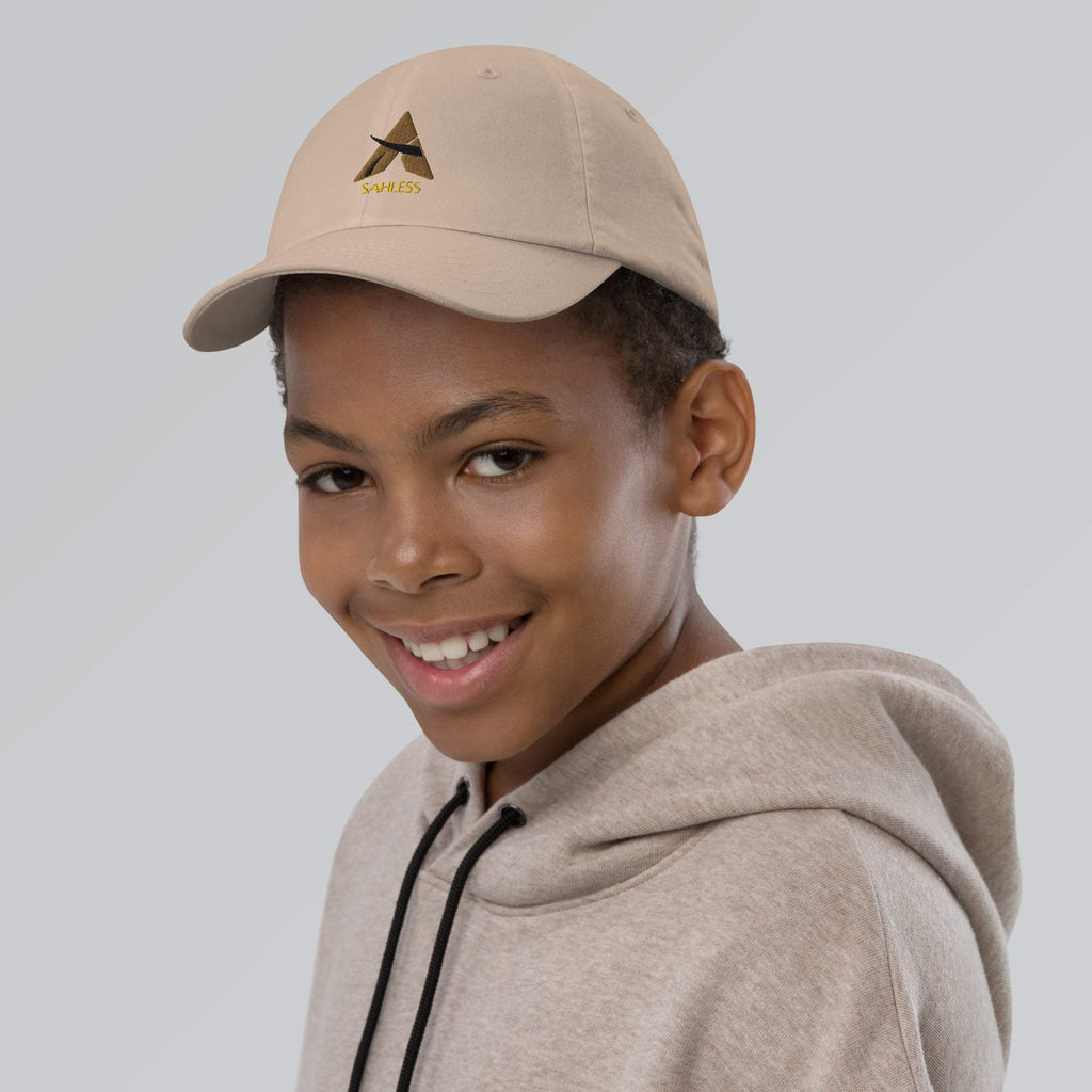 Youth wearing SahLess baseball cap, beige color, with adjustable strap and pre-curved visor for sun protection.