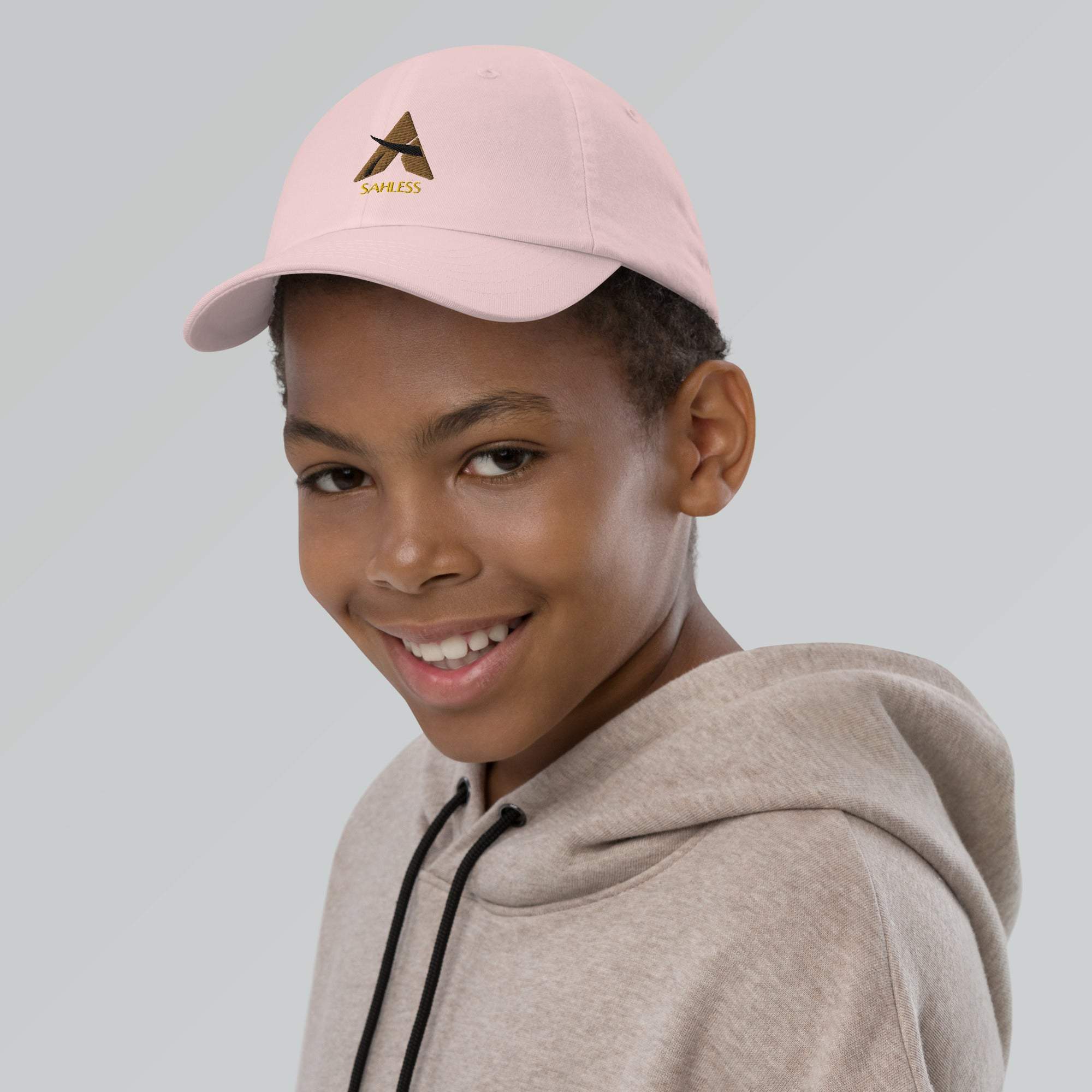 Pink youth baseball cap on smiling child with adjustable strap and SahLess logo.